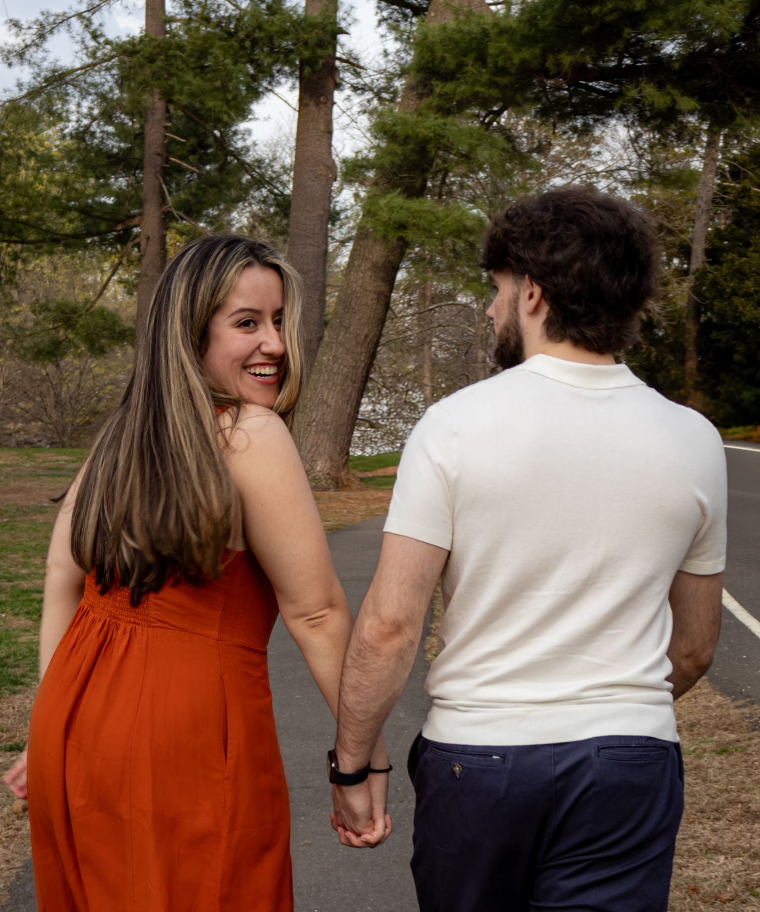 A couple walking together through a park wearing orange and white outfits on a sunny afternoon.
