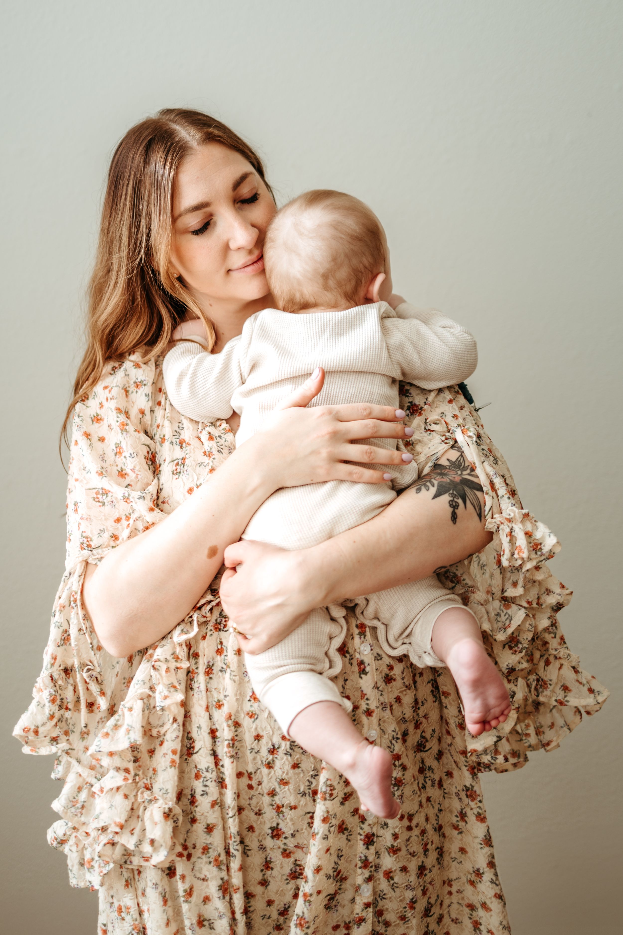 A tender moment captured in a series of photos showing a parent in a floral dress embracing a baby against a neutral background.