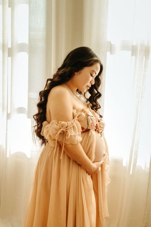 A dreamy portrait series in soft peach tones showing a person in a flowy off-shoulder dress against sheer curtains.