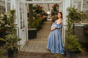 A figure in a flowing blue dress twirls gracefully in a garden courtyard setting with white columns and greenery.