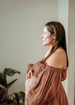 An off-shoulder brown dress is showcased in a minimalist interior setting with natural lighting.