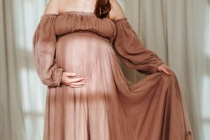 A model poses in a flowing dusty rose gown with delicate draping and elegant movement against a light backdrop.