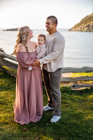 A family shares tender moments together on a grassy coastal cliff overlooking the ocean at sunset.