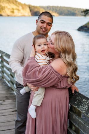 Family enjoying tender moments together on a wooden dock by the water during a sunset photoshoot.