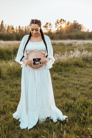 A person in a flowing white dress holds a vintage camera in a golden field at sunset.