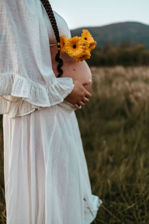 A person in a flowing white dress holds bright yellow sunflowers while standing in a golden field at sunset.