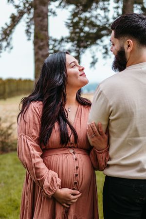 A couple embraces outdoors in a romantic maternity photo session, with the woman wearing a peach-colored dress.