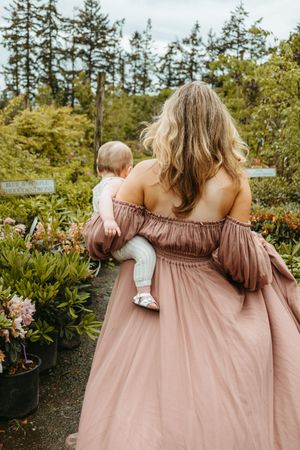 A romantic couple in a garden setting wearing dusty rose and white outfits share an intimate moment among evergreen trees.