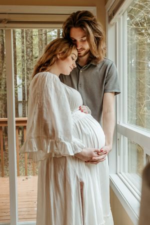 A collage of intimate maternity photos showing a pregnant woman in a white dress by sunlit windows in a rustic setting.