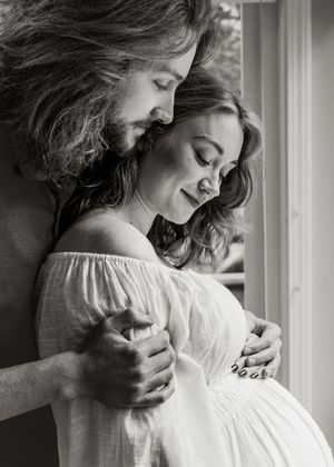 Black and white photo series showing a tender embrace between two people near a window in soft natural light.