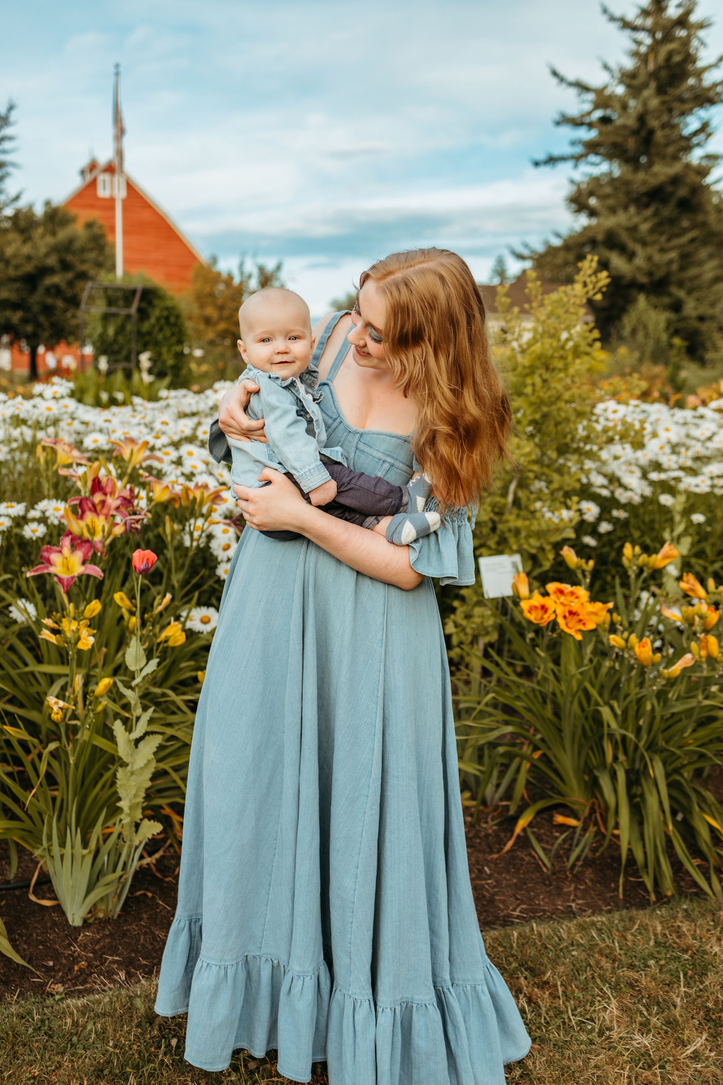 A parent and child wearing matching blue dresses pose together in a garden with blooming flowers and lilies.