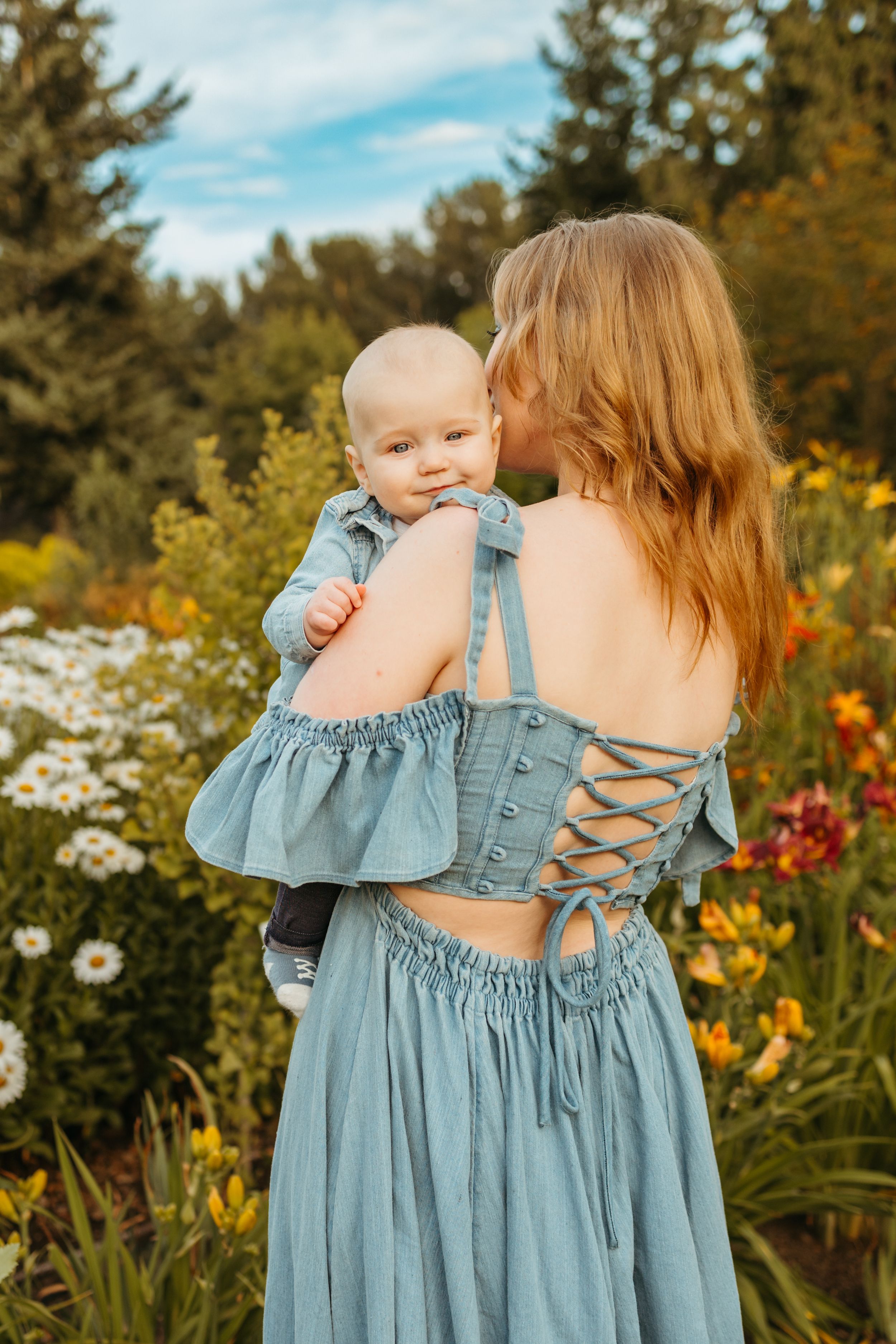 A pair wearing matching light blue dresses with ruffle details stand in a garden with daisies and lilies.