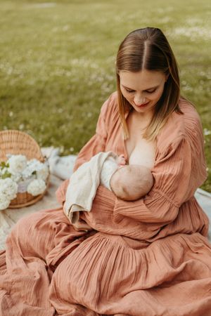 Intimate nursing photography session featuring flowing coral dress on a blanket outdoors.