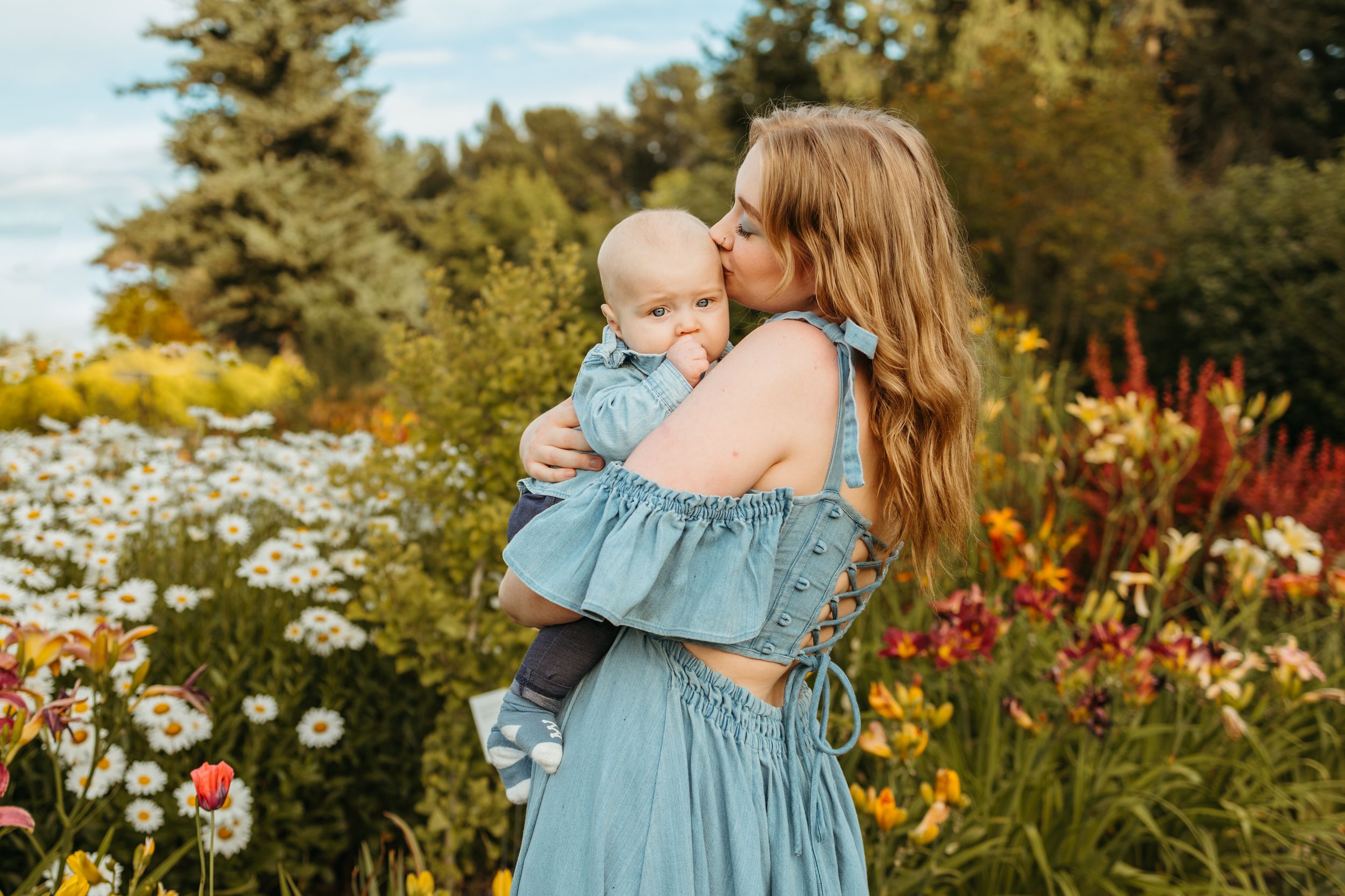 A pair in coordinating blue dresses pose together in a summer garden filled with blooming flowers.