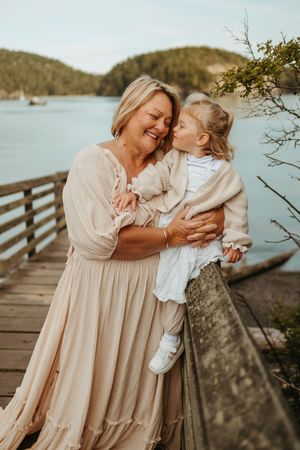 Mother and daughter share tender moments on a wooden dock by the water during a sunset photoshoot.