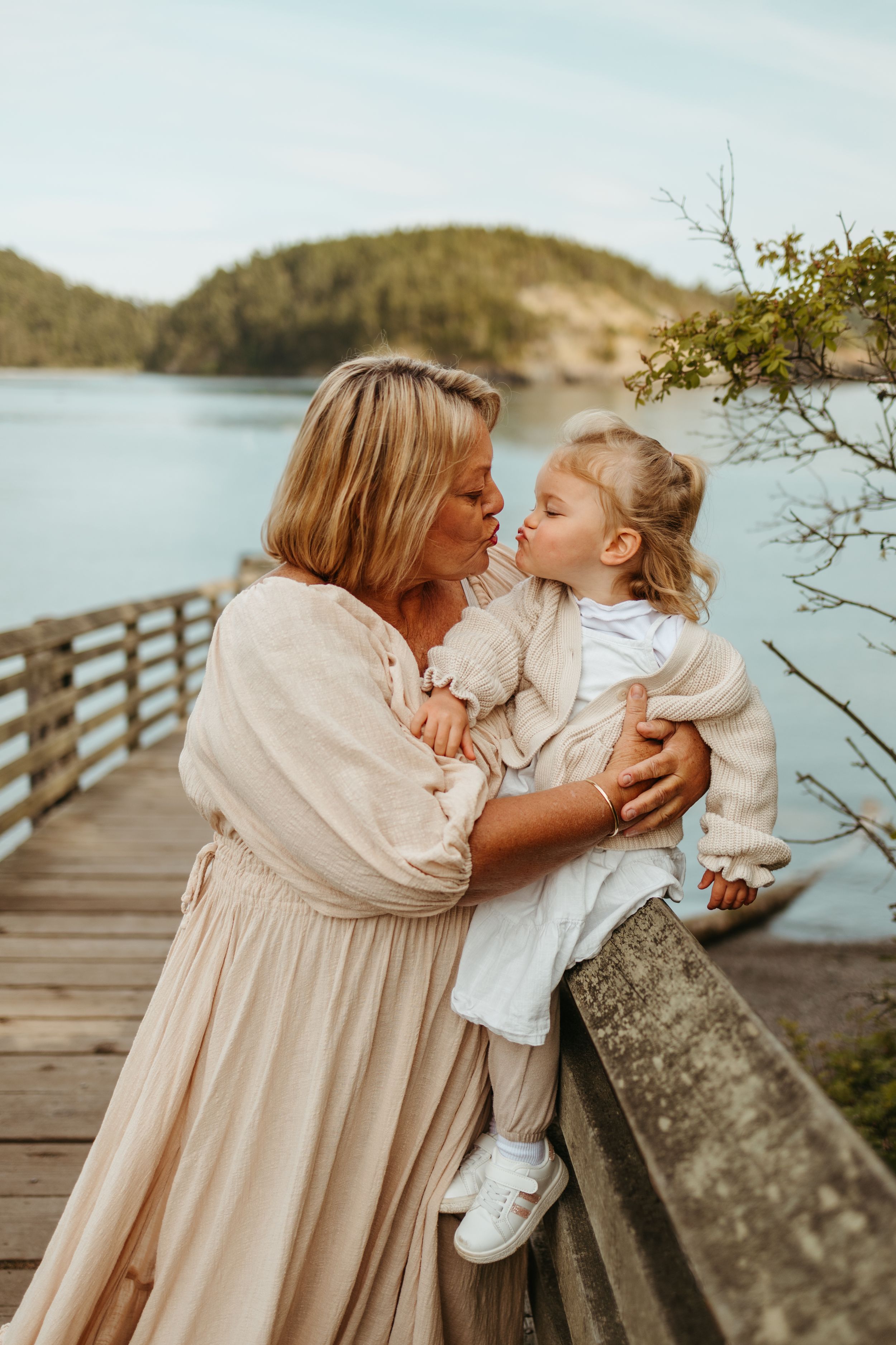 A tender moment between two people wearing cream colored outfits on a wooden boardwalk by a serene lake.