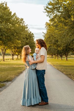 A family shares tender moments together on a tree-lined path during golden hour sunset.