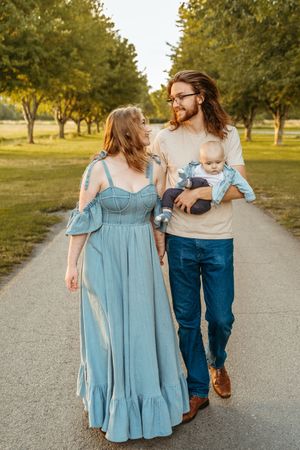 A couple walks hand in hand down a tree-lined path at sunset wearing blue dress and jeans.