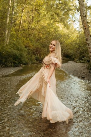 A person in a flowing peach-colored dress twirls gracefully in a shallow stream during golden hour.