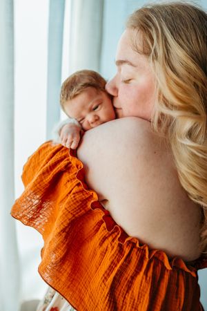 A tender moment captured as a baby in an orange outfit rests peacefully against a parent's shoulder.