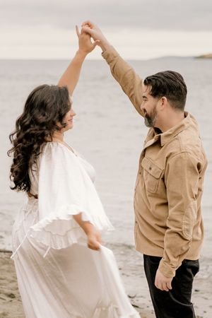 A couple in white and tan outfits dances together on a beach in a romantic sequence of movements.