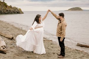 A couple dances together on a rocky beach with ocean and cliffs in the background.