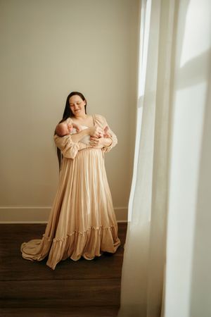 A series of soft, romantic maternity photos featuring a flowing champagne-colored dress in a sunlit room with white walls.