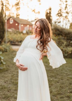 A figure in a flowing white dress twirls gracefully in a sunlit garden during golden hour.