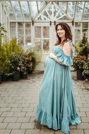 A person in a flowy turquoise dress poses in front of a greenhouse in a series of lifestyle photos.