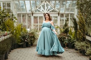 A turquoise dress flows elegantly in a greenhouse setting with natural light streaming through glass panels.