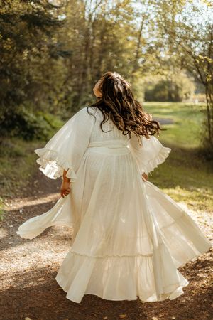 A flowing white vintage-style dress twirls in a sunlit autumn forest setting, creating an ethereal motion effect.
