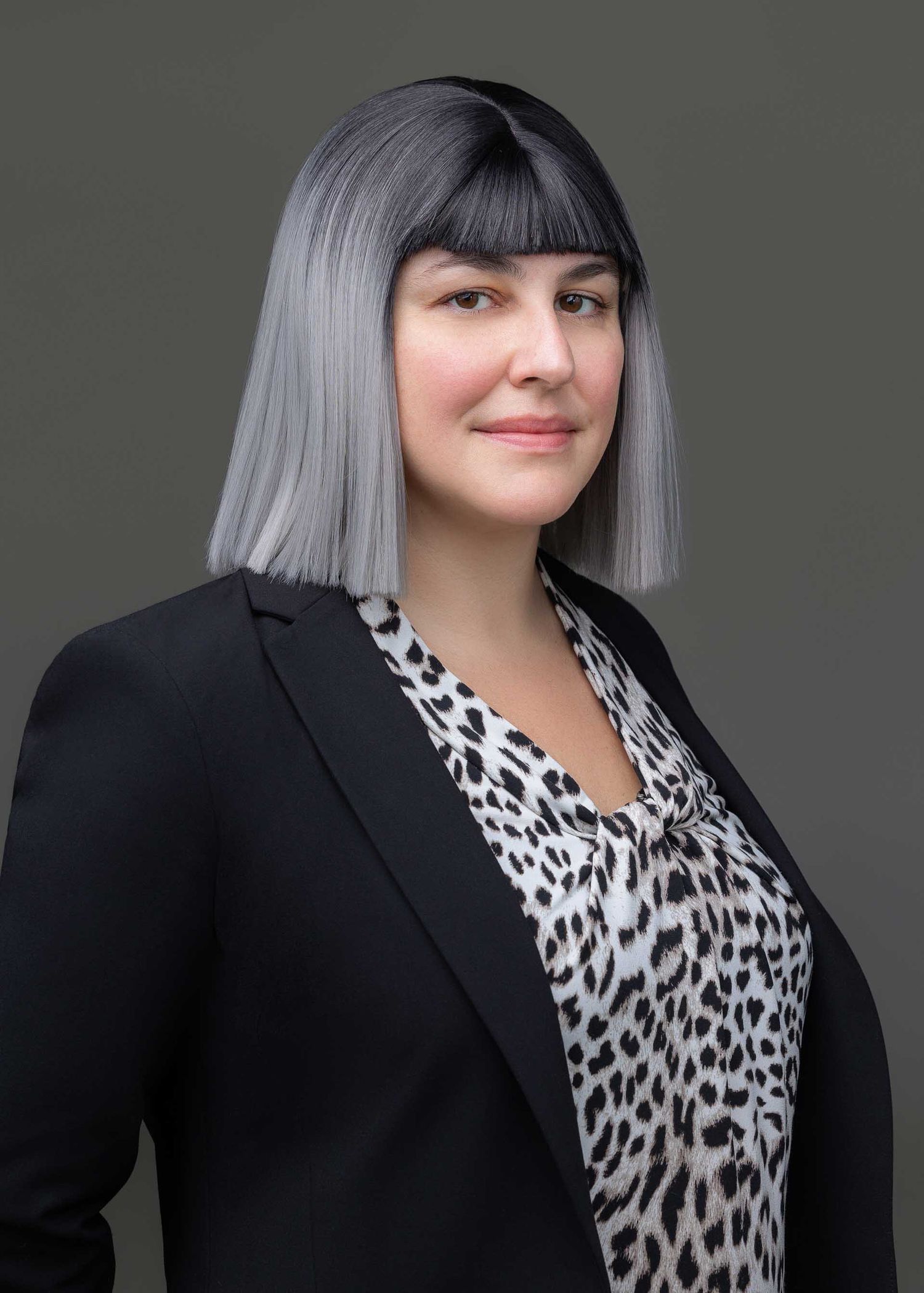 Professional headshot of a gray-haired woman wearing a black blazer against a dark studio background.