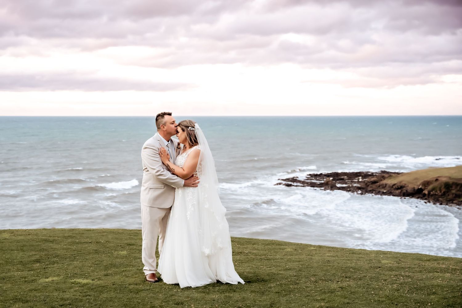 Couple standing on an ocean cliff during sunset in Maui while wearing wedding attire.