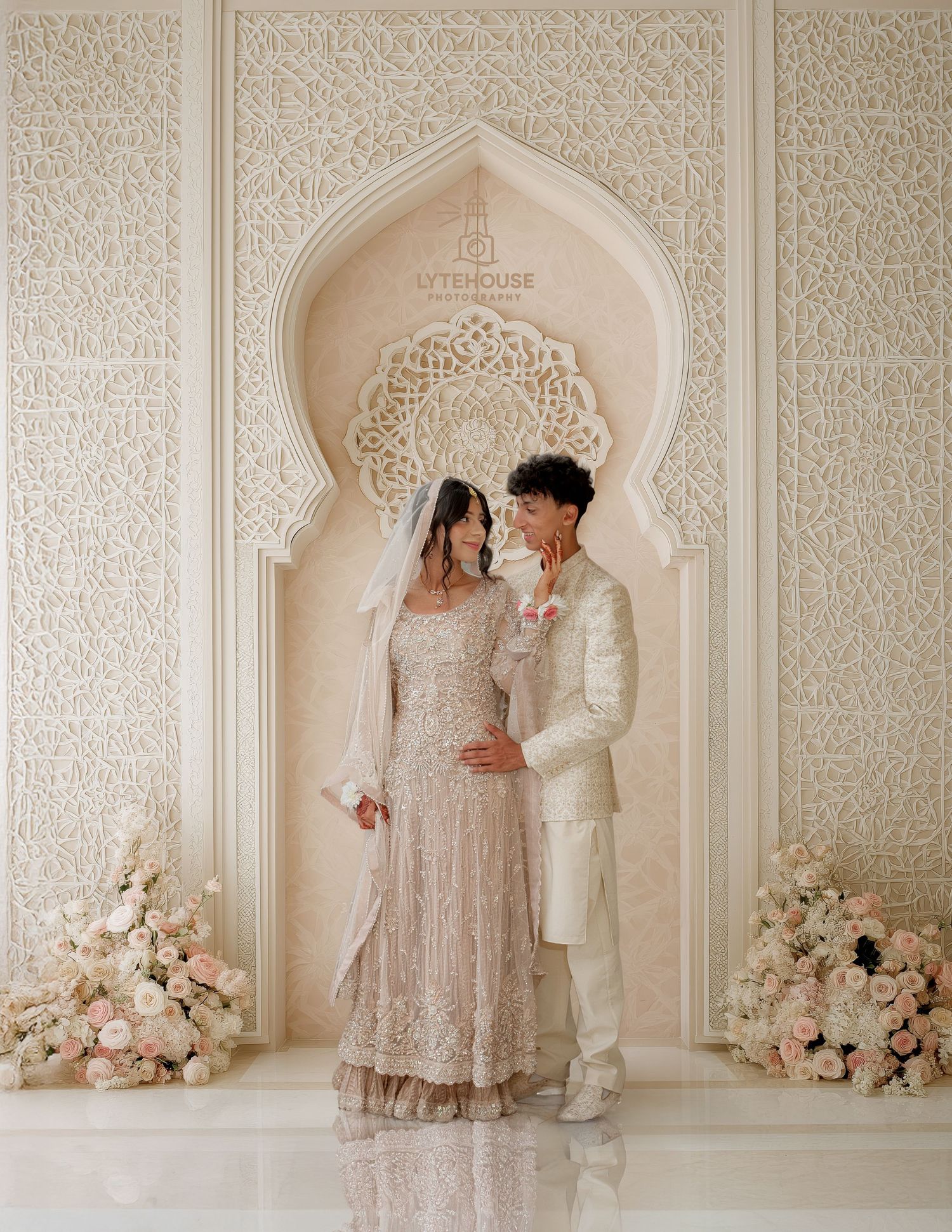 A romantic scene in an elegant white and beige room with ornate walls and floral arrangements.