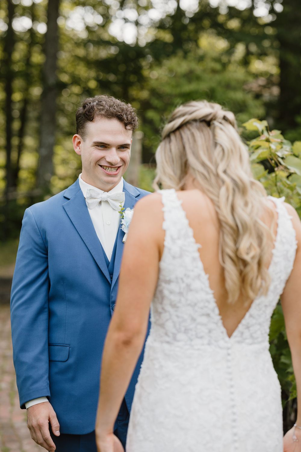 A bride and groom share a sweet first look moment in a sun-dappled forest setting.