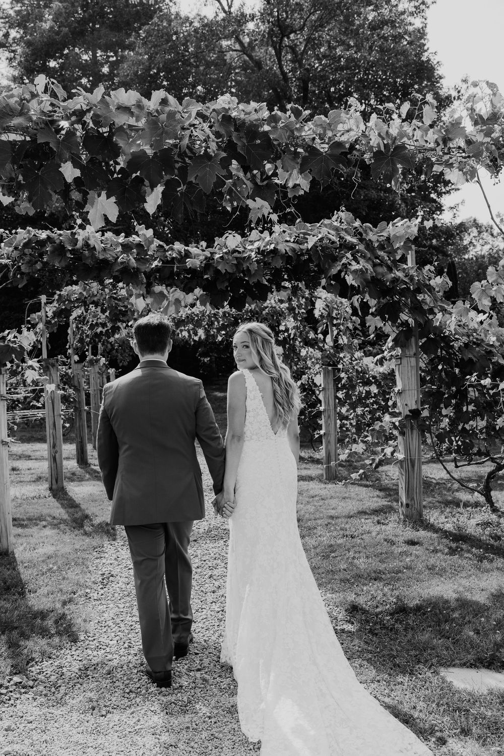 A couple walks hand in hand through a scenic orchard path in black and white wedding attire.