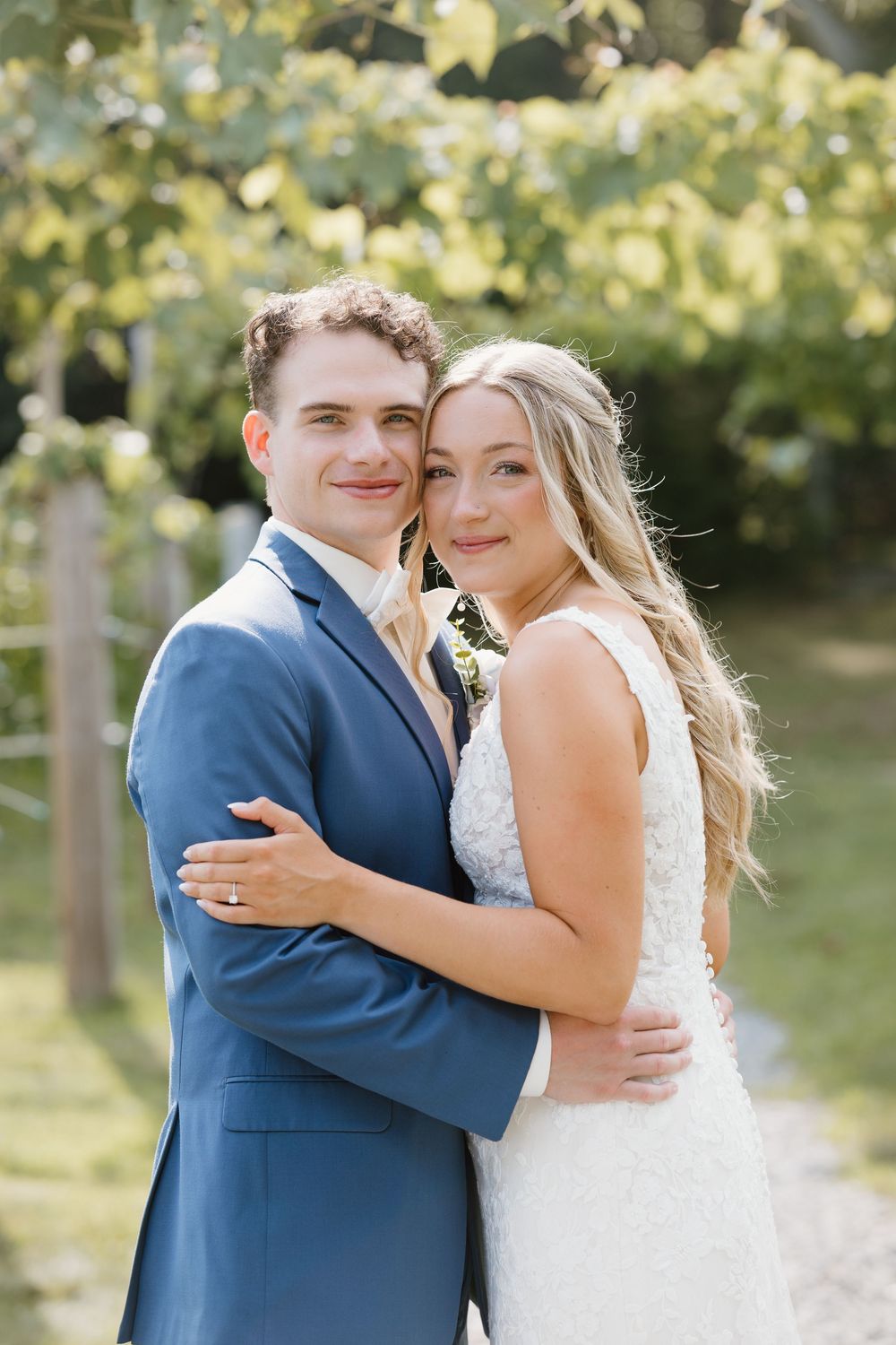 A couple embraces in joyful celebration during their outdoor wedding surrounded by sunlit trees and foliage.