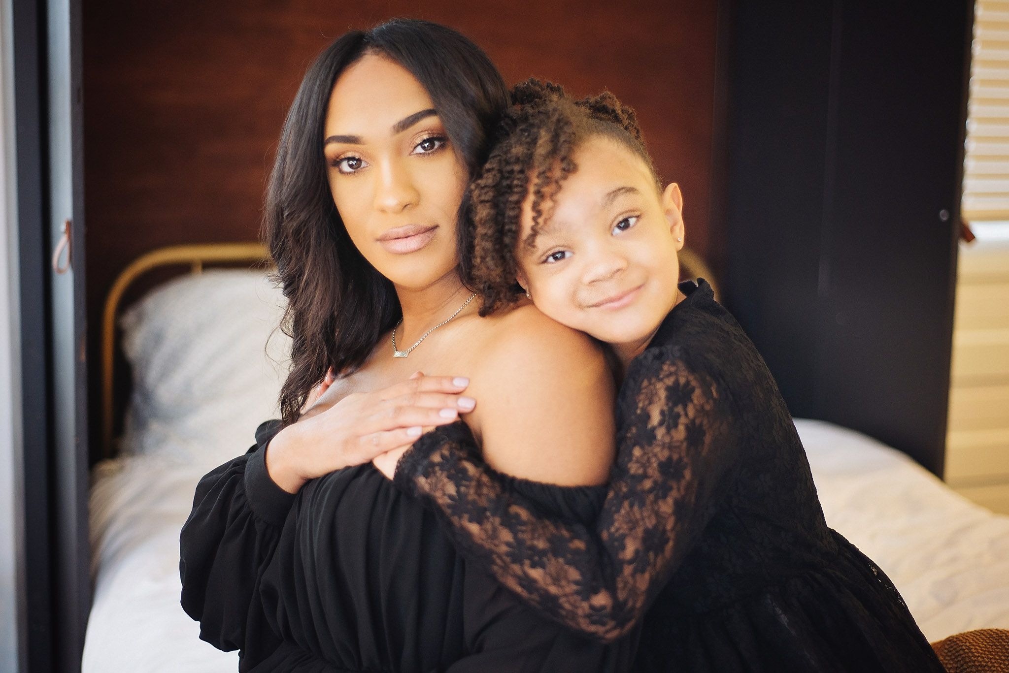 Woman and young girl in matching black outfits sharing a warm embrace indoors.