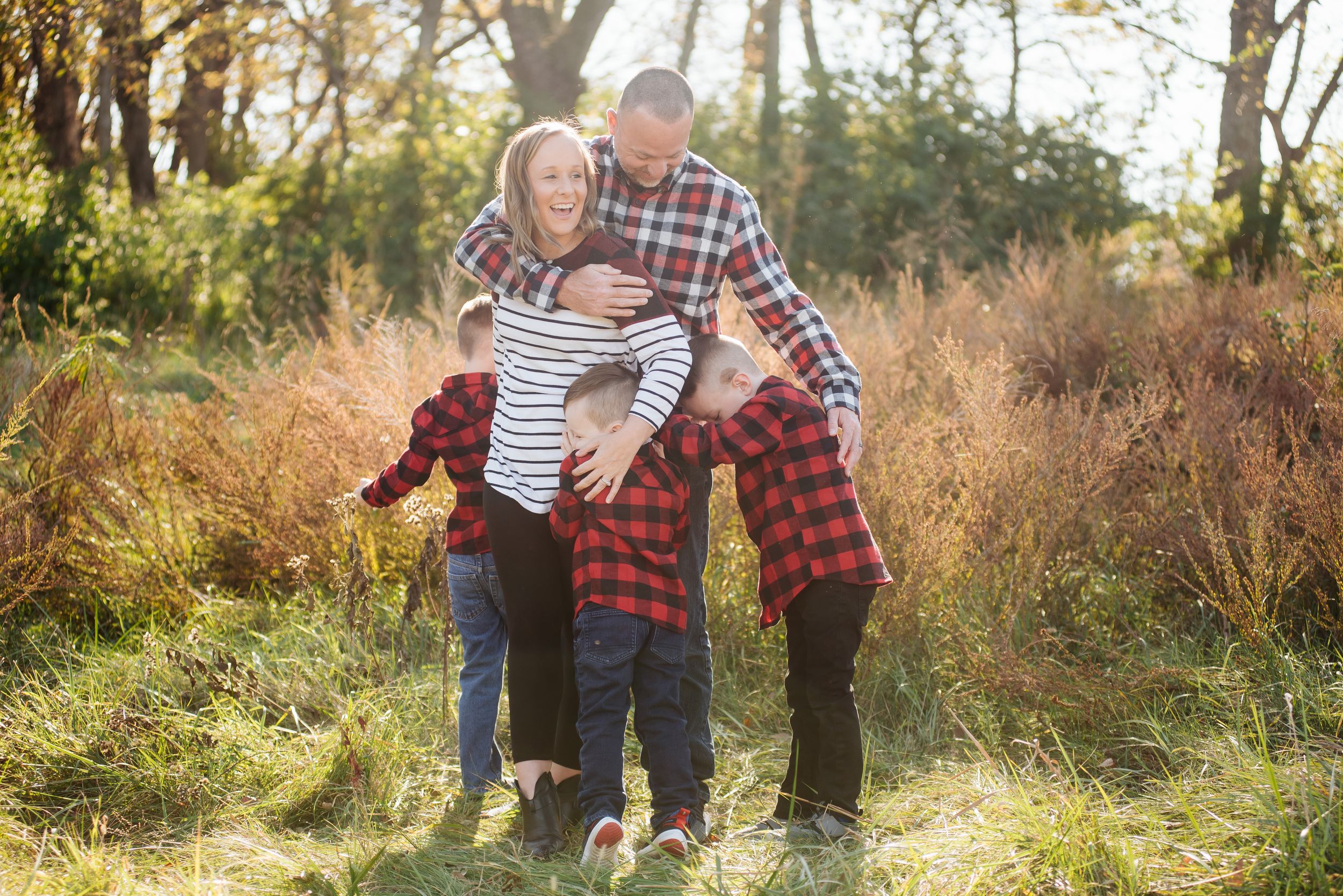 Joyful family of four in matching red plaid shirts playing and hugging in a sunny autumn meadow.