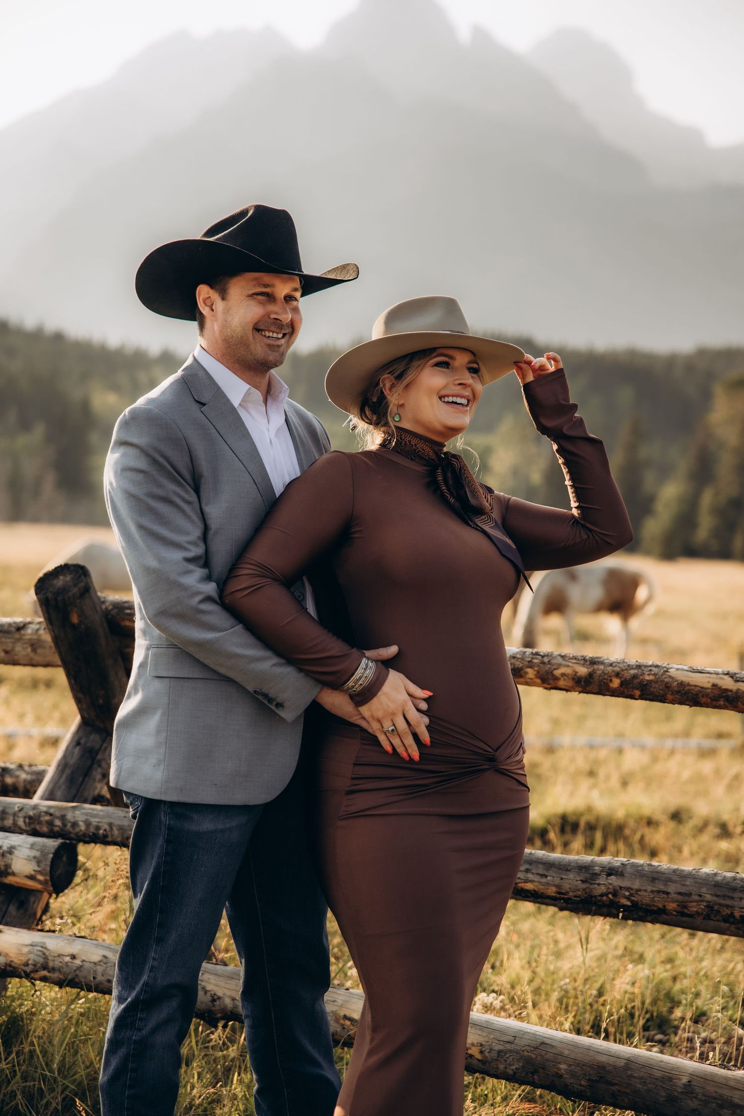 A couple shares an intimate moment during their maternity photoshoot in a rustic mountain setting at sunset.