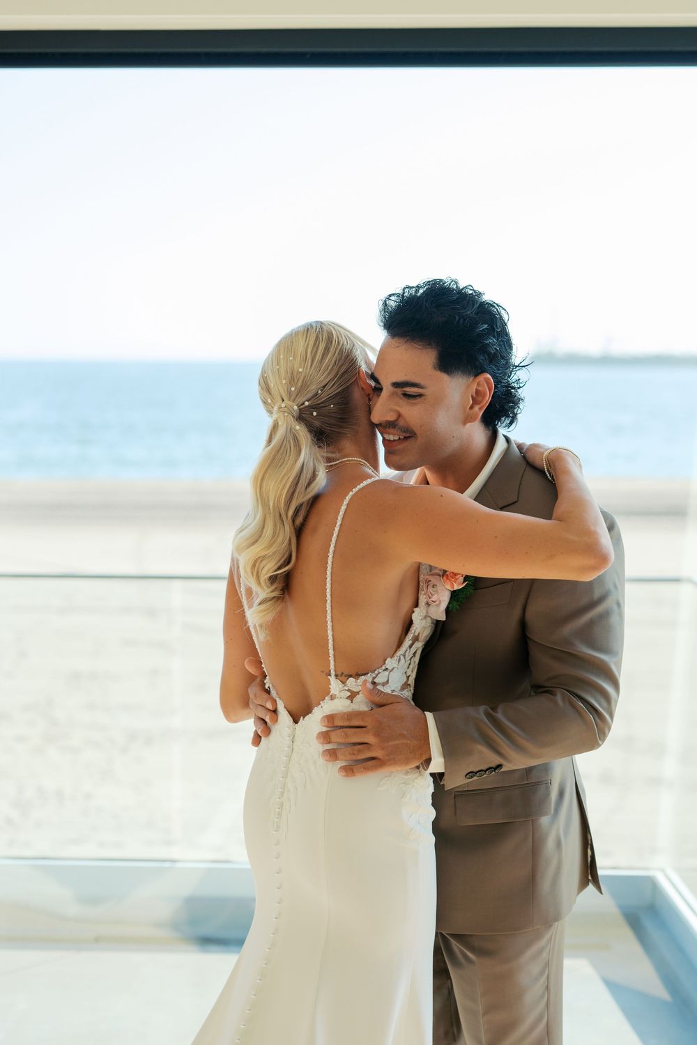 A couple shares a tender beachside hug during a seaside wedding celebration as ocean waves roll in the background.
