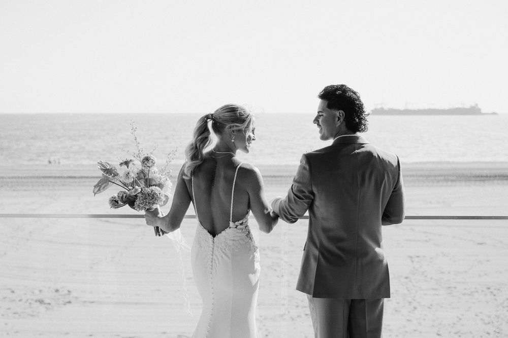 Black and white artistic photos of a couple walking together on a sandy beach holding hands against a dreamy landscape.
