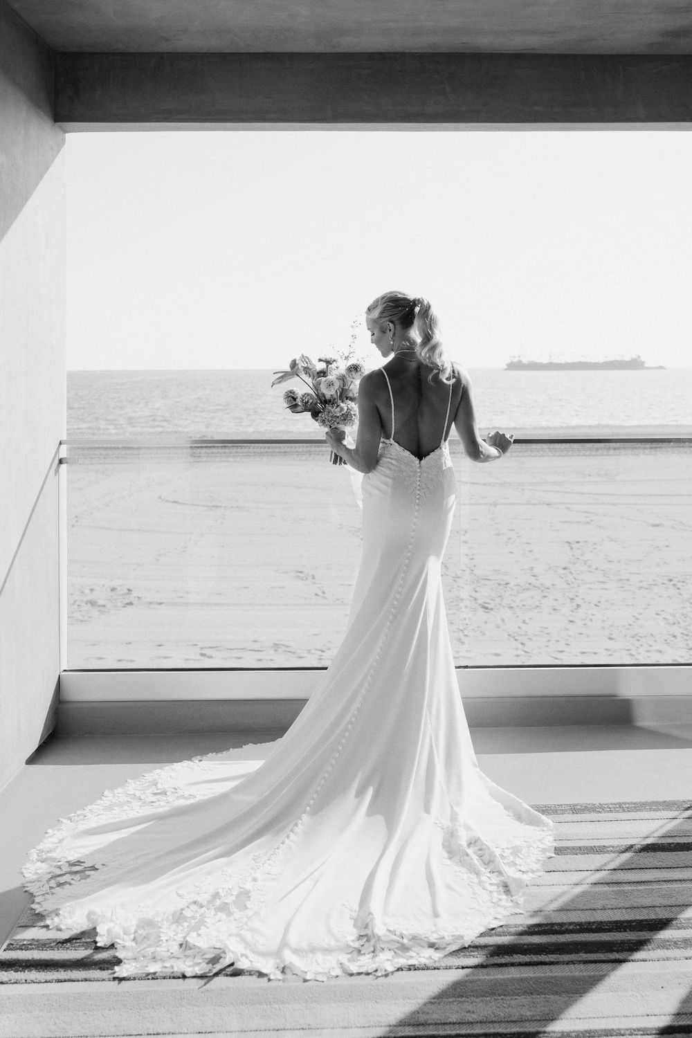 Black and white series showing a wedding dress train flowing elegantly across a wooden boardwalk near the beach.