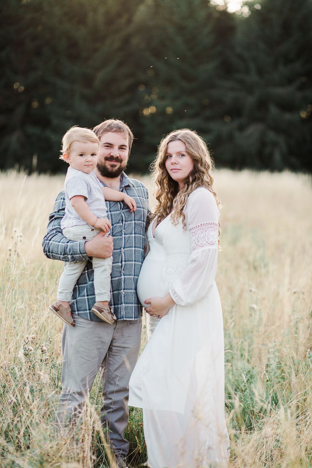 Family wearing white and plaid standing together in a golden field at sunset.