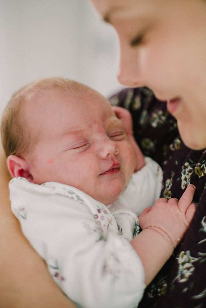 Gentle moment with sleeping newborn baby in white clothing.