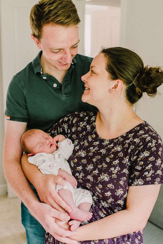 Parents in casual attire share loving moments with their newborn baby in a bright indoor setting.
