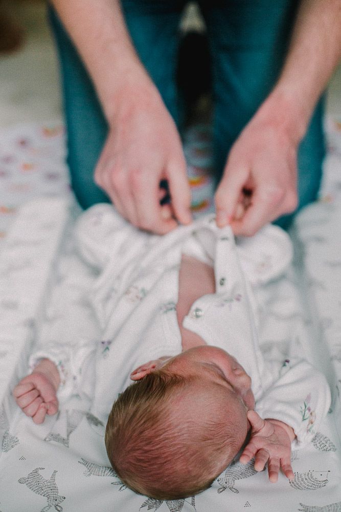 Hands gently placing a newborn baby on a patterned white blanket.