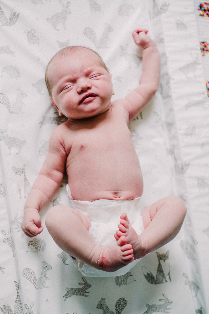 Happy newborn baby lying on a white patterned blanket with animal prints.