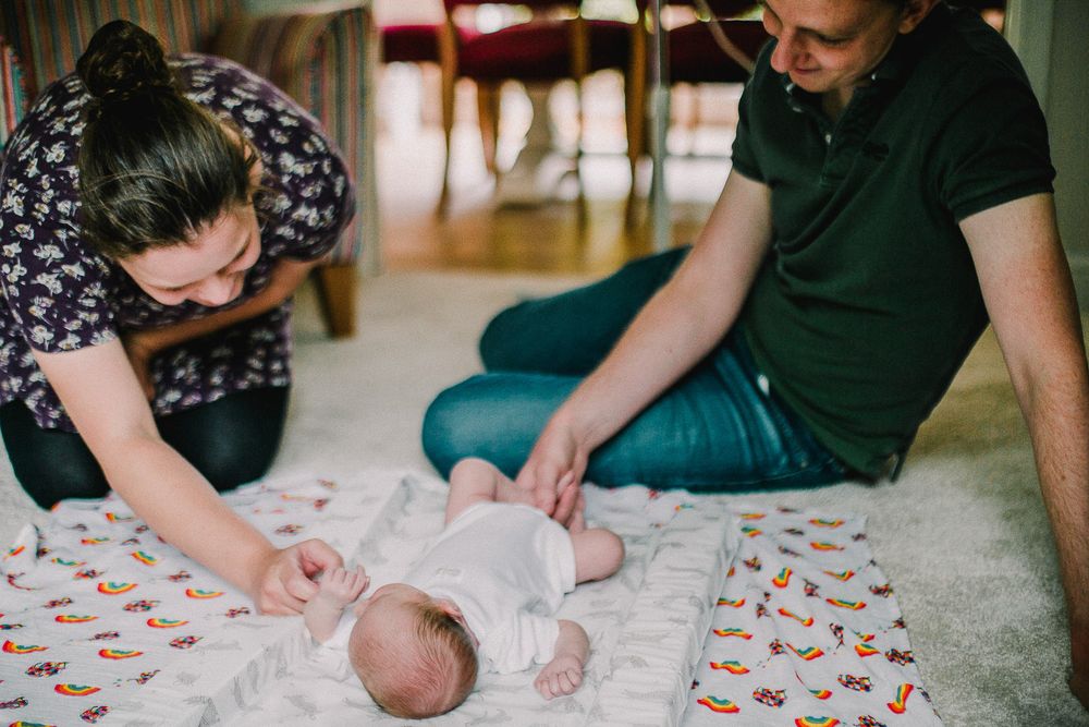 Family gathering around a newborn baby on a colorful patterned blanket.
