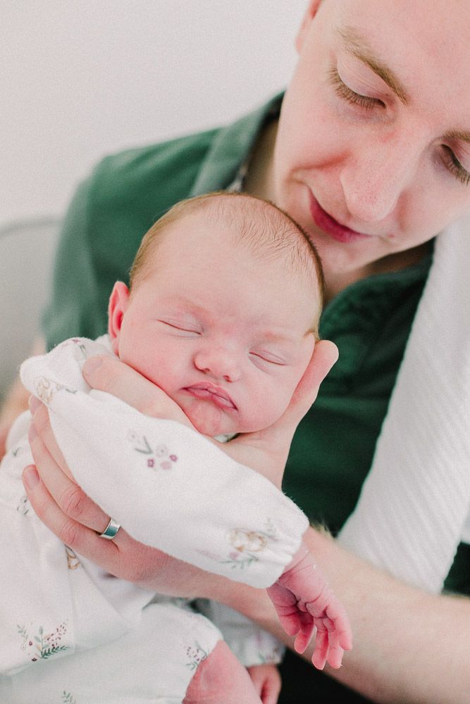 Close-up view of sleeping newborn in white outfit being held gently.